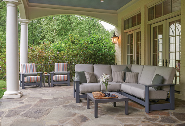 Outdoor patio furniture set with gray sectional sofa, striped armchairs, and coffee table on a stone patio in CT
